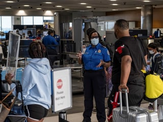 Sicherheitspersonal weist Reisende bei den Sicherheitskontrollen am Flughafen ein.