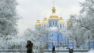 Ältere Frau stapft durch den Schnee vor einer Kathedrale mit goldenen Kuppeln. Ältere Frau stapft durch den Schnee vor einer Kathedrale mit goldenen Kuppeln.