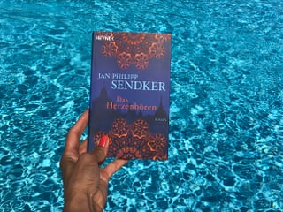 Annette König hält das Buch von Jan-Philip Sendker: «Das Herzhören» vor blaues Wasser
