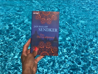 Annette König hält das Buch von Jan-Philip Sendker: «Das Herzhören» vor blaues Wasser Annette König hält das Buch von Jan-Philip Sendker: «Das Herzhören» vor blaues Wasser