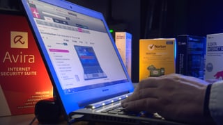 Ein Mann arbeitet an einem Laptop, darum herum stehen verschiedene Antivirenschutz-Programme.