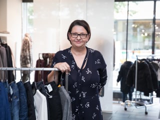 Eine Frau steht vor einer Garderobenstange in einem Kleiderladen.
