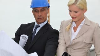Ein Architekt mit Bauhelm zeigt einer jungen Frau Baupläne.