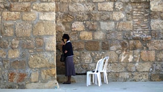 Eine Frau steht an der Klagemauer. Hinter ihr stehen zwei weisse Plastikstühle.