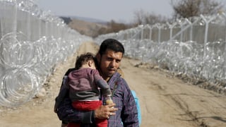 Ein Flüchtling an der griechisch-mazedonischen Grenze mit einem Kind auf dem Arm. 