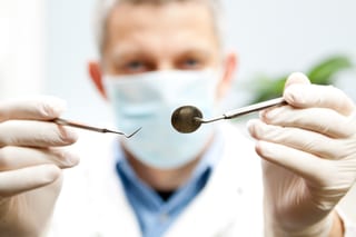 Ein Zahnarzt hält einen Spiegel und ein Diagnosewerkzeug vor die Kamera.