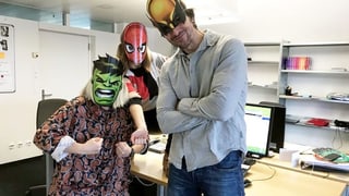 Drei unglaublich attraktive Superhelden posieren in einem unglaublich unattraktiven Büro.