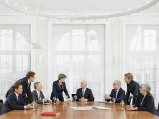 Die Bundesrätinnen und Bundesräte stehen um einen Tisch herum und diskutieren, Dokumente in der Luft