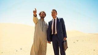 Tom Hanks als Alan Clay mit seinem Fahrer Yousef stehen in der Wüste.