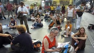 Passanten sitzen auf dem Perron am Boden und vertreiben sich die Zeit mit Lesen. Passanten sitzen auf dem Perron am Boden und vertreiben sich die Zeit mit Lesen.