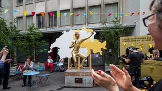Ein golden gelkeiderter Mann steht vor einer Schweizerkarte.