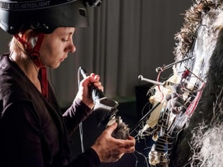 Eine Frau mit Helm vor einer verkablenten Fläche aus unterschiedlichen Materialen. Sie hält ein Gerät daran. Eine Frau mit Helm vor einer verkablenten Fläche aus unterschiedlichen Materialen. Sie hält ein Gerät daran.