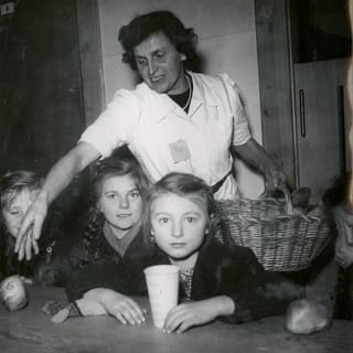 Eine Frau steht hinter Kindern, die an einem Tisch sitzen. Eine Frau steht hinter Kindern, die an einem Tisch sitzen.