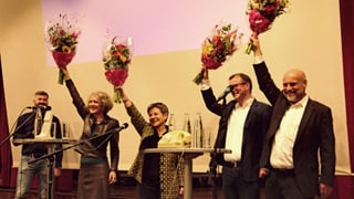 vier KandidatInnen auf Bühne strecken Blumensträusse in die Luft