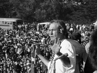 Ein Mann spricht vor einem Mikrophon zu einer Menschenmenge.