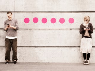 Ein Mann und eine Frau stehen an einer Wand und schauen jeweils auf einen Bildschirm. Eine Linie aus rosa Punkten verbindet ihre Körper. Ein Mann und eine Frau stehen an einer Wand und schauen jeweils auf einen Bildschirm. Eine Linie aus rosa Punkten verbindet ihre Körper.