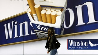 Zigarettenwerbung auf einem Plakat, davor läuft eine Passantin vorbei. 