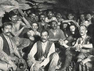 Nach dem Durchstich im Lötschbergtunnel: Viele Männer in dreckiger Arbeitskleidung schauen gebückt in die Kamera. 