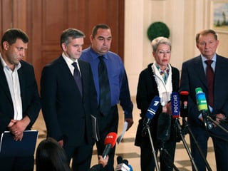 Vier Männer und eine Frau stehen nebeneinander vor Mikrofonen.