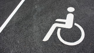 Ein Behinderten-Zeichen auf einer schwarzen Strasse.