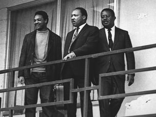 Drei Männer in Anzügen stehen auf einem Balkon