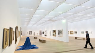 Ein Mann geht durch helle Ausstellungsräume mit Kunstwerken an den Wänden und am Boden Ein Mann geht durch helle Ausstellungsräume mit Kunstwerken an den Wänden und am Boden