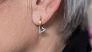 Nahaufnahme eines Ohrs: An einem Ohrring hängt ein Dreieck.