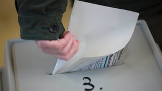 Eine Hand steckt einen Wahlzettel in eine Wahlurne (keystone)
