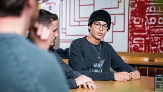 Drei junge Männer nebeneinander an einem Tisch, in ein Gespräch vertieft Drei junge Männer nebeneinander an einem Tisch, in ein Gespräch vertieft