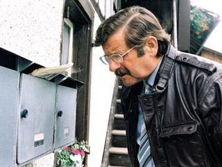 Ein Mann mit Brille und Lederjacke steht vor einen Briefkasten.