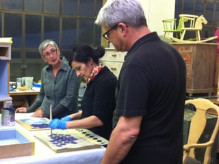 Daniel, Patrizia und Anet: Anet stupft mit einem Pinsel Farbe auf das Holz.