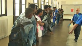 Eritreer stehen bei der Einreise an einem Gepäcktisch und folgen den Instruktionen der Zollbehörden.
