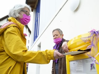 Frauen werfen das Stimmcouvert in einen gelben Postkasten.