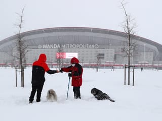 Spaziergänger mit Hunden im Schnee vor dem Stadion von Atletico Madrid.
