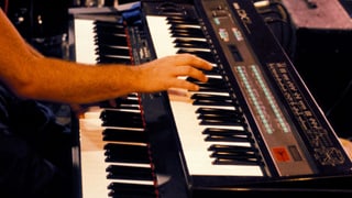 Eine Hand greift in die Tasten eines Synthesizers mit dem Label DX7.