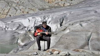 Ein Mann sitzt mit Gitarre an einem Gletscher.