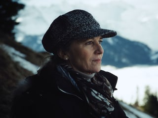Porträt Sabine mit Kappe mit Bergen mit Schnee im Hintergrund.