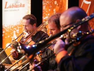 Trompeten und Posaunen-Spieler vor Kulisse während Auftritt.