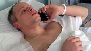 Mann liegt im Spital und telefoniert mit dem Handy. 