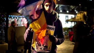 Mann mit Flagge und Satire-Magazin an Demo.