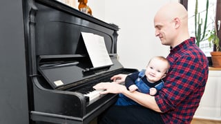 Ein Mann sitzt am Klavier mit Baby
