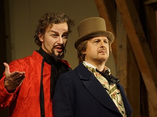 Zwei Schauspieler, einer mit roter Robe, der andere mit altertümlichem Hut