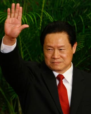 Ex-Sicherheitschef Zhou Yongkang winkt mit der rechten Hand. Er trägt einen Anzug mit roter Krawatte.