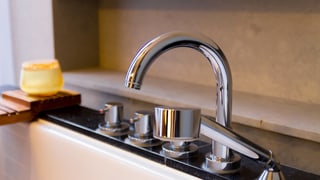 Auf dem Rand einer neuen Chromstahlbadewanne steht eine Kerze