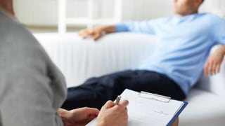 Person mit Schreibblock berät Person auf Sofa.