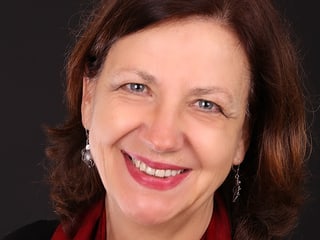 Karin Krieger trägt einen roten Schal und lächelt in die Kamera.