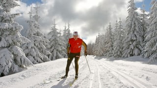Langläufer in roten Oberteil und schwarzen Hosen in schneebedeckter Landschaft