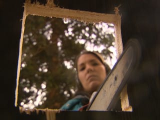 Künstlerin mit Kettensäge schneidet ein Fenster in eine Wand.