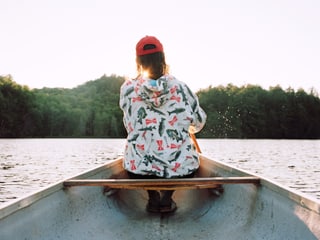 Rückenansicht eines Mannes, der in einem Boot auf einem See sitzt.