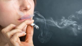 Eine Frau führt eine brennende Zigarette an ihren Mund